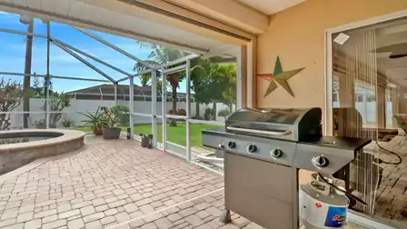 Modern gas grill in the sheltered patio area with view of the garden and pool, fully enclosed by a breathable screen structure.