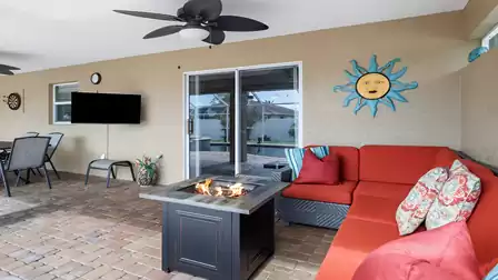 Cozy lounge area with red sectional sofa and fire table on the covered terrace, with a view of the pool and screened outdoor area in the background.