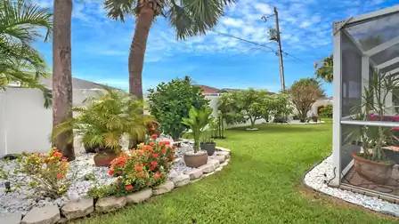 Tropical garden area with palm trees, blooming plants, and a well-kept lawn next to the screened pool enclosure.