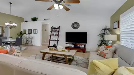 Helles Wohnzimmer mit gemütlichen Sofas, Fernseher, Deckenventilator und dekorativem Bücherregal in einem Ferienhaus in Cape Coral.