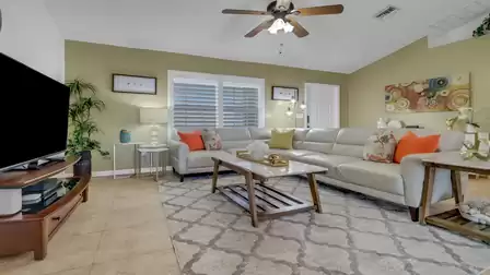 Bright living room with large cream-colored leather sofa, decorative pillows, ceiling fan, and stylish coffee table on patterned rug