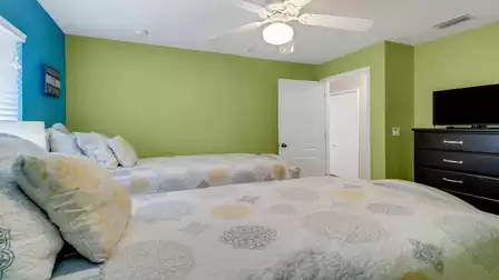 View into a colorful bedroom with two twin beds, TV dresser and vibrant green and blue walls