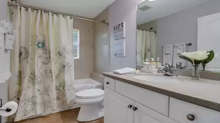 Bright bathroom with bathtub, floral shower curtain and large mirror above the sink