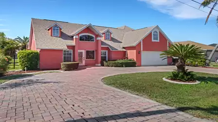 Exterior view of Villa Kasar in Cape Coral with well-kept front yard, palm trees, large driveway, and pink facade.