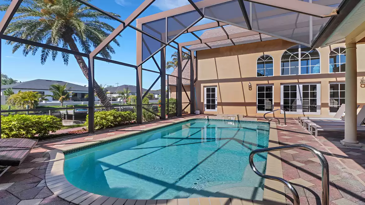 Screened-in pool area of Villa Kasar with palm tree view, sun loungers, and canal access in the background.