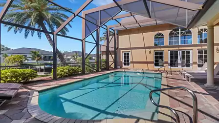Screened-in pool area of Villa Kasar with palm tree view, sun loungers, and canal access in the background.