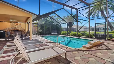 Sun loungers by the screened pool, covered dining area with stone fireplace in the background