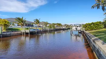 Tranquil canal with boat lift and palm trees, lined with well-kept lawns and residential homes.