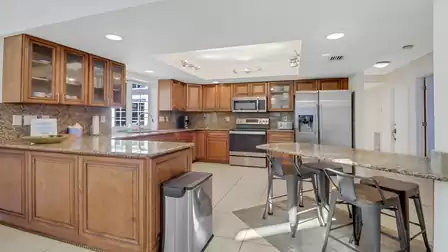 Fully equipped kitchen with granite countertops, wooden cabinets, bar area with stools, and modern stainless steel appliances.