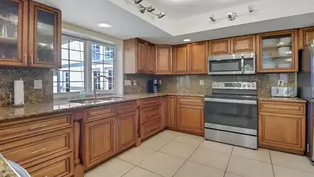 Modern kitchen with granite countertops, wooden cabinets, stainless steel appliances, and a large window view to the outside.