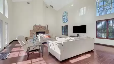 Spacious living room with high ceilings, bright seating area, natural stone fireplace, and flat-screen TV.