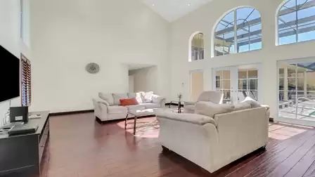 Bright living room with high ceilings, large arched windows, and direct access to the covered patio with pool.