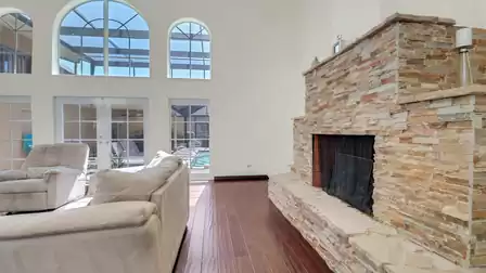Living area featuring a natural stone fireplace, floor-to-ceiling windows, and view of the covered pool area.