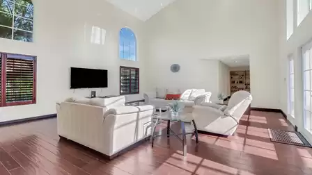 Bright and spacious living room with high ceilings, cozy sofas, a TV, and direct access to the patio.