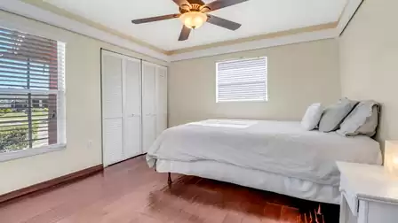 Bright bedroom with wooden flooring, ceiling fan, and large window allowing natural light.