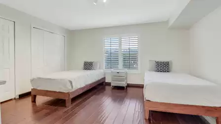 Bright bedroom with two twin beds, wooden flooring, and window with shutters.