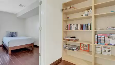 Single bed with wooden frame next to a shelf filled with books, board games, and puzzles - perfect for cozy indoor time.
