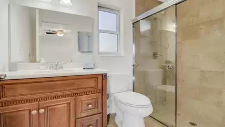 Bright bathroom with large glass shower, wooden vanity and mirror.