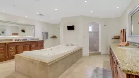 Spacious bathroom with whirlpool tub, double sinks, walk-in shower, and wall-mounted TV.