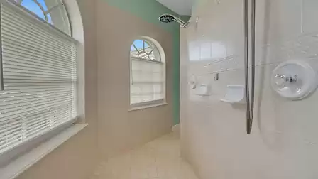 Spacious walk-in shower in the master bathroom with two arched windows and elegant tile finish.