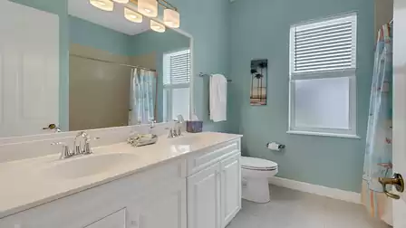 Bright bathroom featuring double sinks, a bathtub with shower, and cheerful coastal décor.