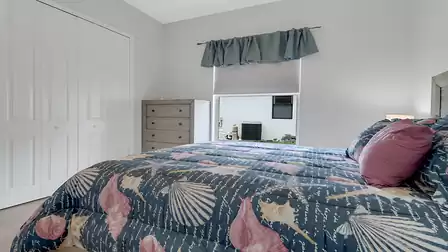 Bedroom with seashell-pattern bedding, dresser, closet doors, and window to office