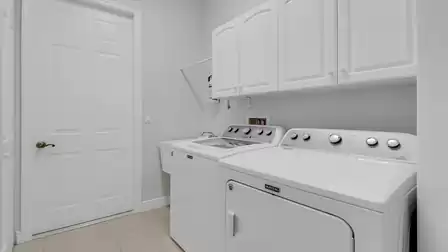 Bright laundry room with washing machine, dryer, and ample storage in white overhead cabinets.