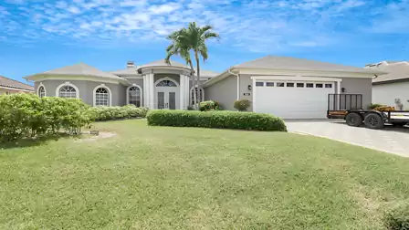 Exterior view of Villa Lavinia featuring a manicured front yard, palm trees, and a classic columned entrance in Cape Coral