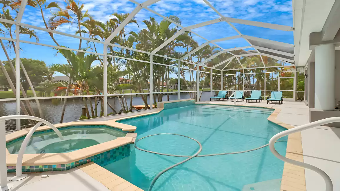 Screened pool area with spa, sun loungers, and canal view - surrounded by tropical greenery