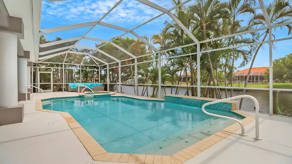 View of the spacious pool and spa area with lounge seating and palm trees by the waterfront