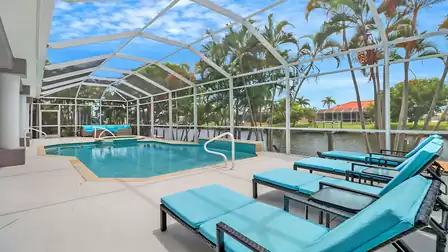 Row of turquoise sun loungers by the pool with views of palm trees and water.