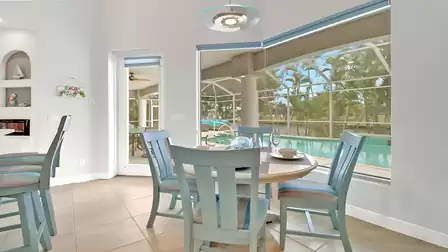 Bright breakfast nook with round table and blue chairs, view of the pool and canal.