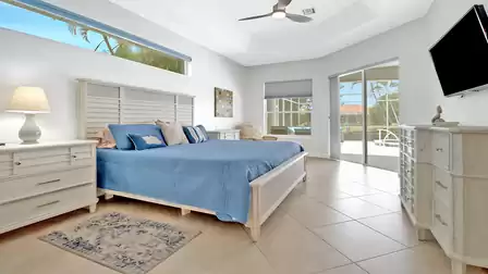 Cozy master bedroom featuring a king-size bed, light wood furniture, and direct access to the pool area.