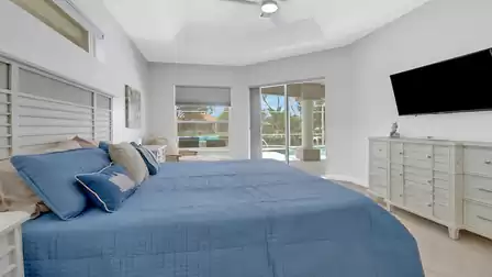 Master bedroom facing the adjacent bathroom, featuring coastal wall art and modern natural-tone floor tiles.