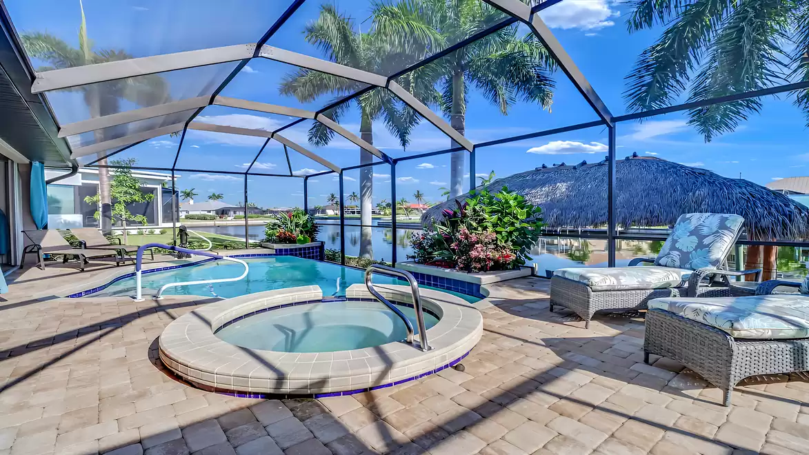 Pool area with integrated spa, sun loungers, and tropical plants by the canal.