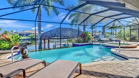 View of the inviting pool area with spa, sun loungers and tropical landscaping under the screened lanai.