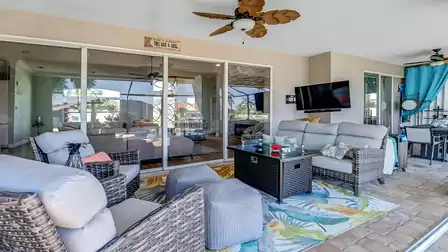 Outdoor living room with TV, ceiling fans and access to the fully equipped summer kitchen