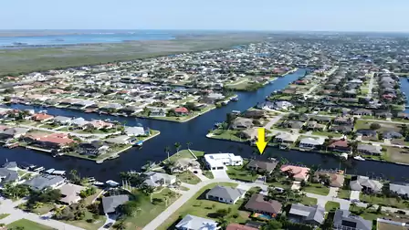 Wide-angle shot of the peaceful Cape Coral neighborhood with canals; yellow arrow indicates the villa’s location.