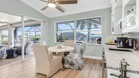 Breakfast area with four upholstered chairs, a round wooden table, and direct view of the canal through large windows and sliding doors to the terrace.