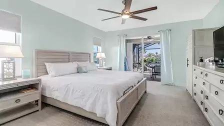 Master bedroom with king-size bed, nightstands, ceiling fan, and access to the covered terrace with water views.