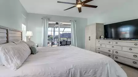 Bedroom with dresser, large flat-screen TV, light curtains, and direct view of the outdoor area.