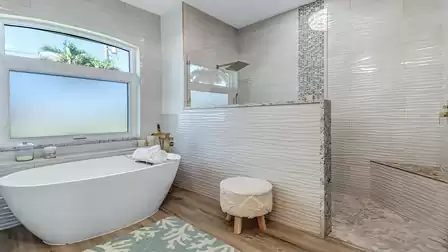 Freestanding bathtub with garden view and walk-in shower featuring a glass partition and natural stone tiles.