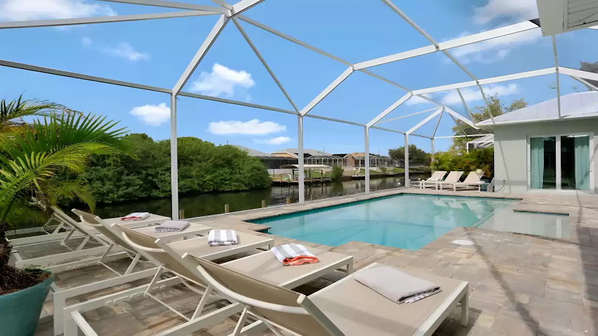 Spacious, screened-in pool area of Villa Cupido with sun loungers, direct canal view, and tropical landscaping.