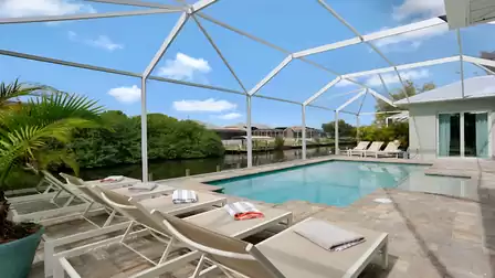 Spacious, screened-in pool area of Villa Cupido with sun loungers, direct canal view, and tropical landscaping.