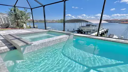 Spa with view of the canal and covered boat dock, framed by sparkling pool water and screen.
