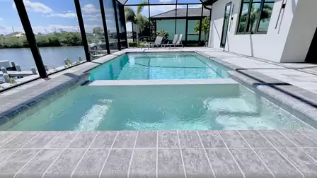 View from the spa across the elongated pool with modern travertine surround and screen enclosure.