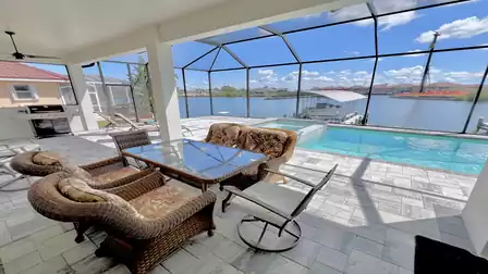 Covered patio with dining area, lounge furniture, and stunning views over the pool and canal.