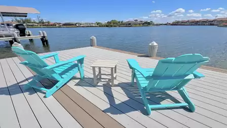 Two turquoise Adirondack chairs with a side table on the sun deck overlooking the water.