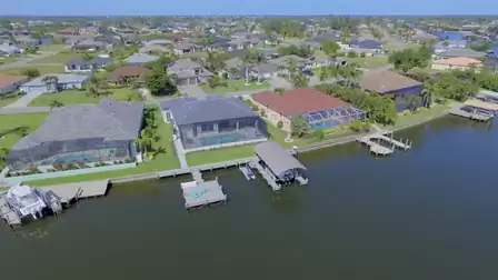 Aerial view of residential neighborhood with canal access, private boat dock, and screened pool area.