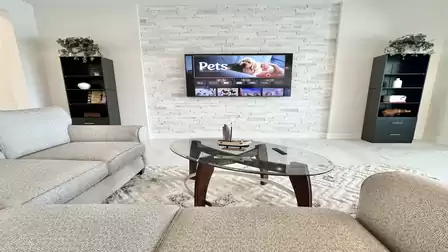 Stylish living area with wall-mounted TV, glass table, and two shelves for decor or books.